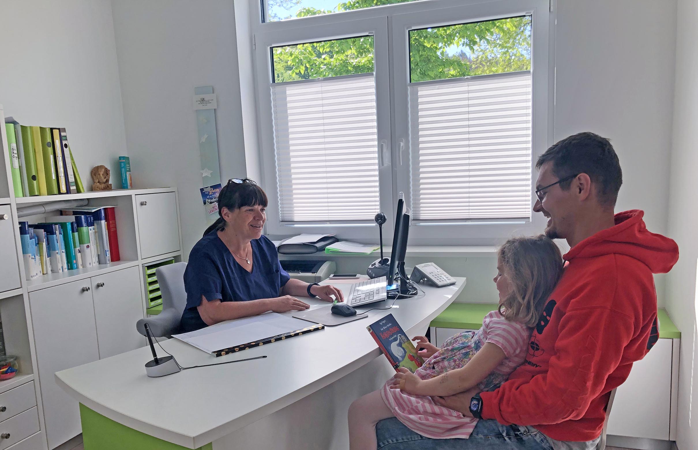 Vertrauensvolle Beratung durch Frau Dr. med. Regina Kreutz – ein Patient mit seinem Kind im Arm lächelt während des Gesprächs.