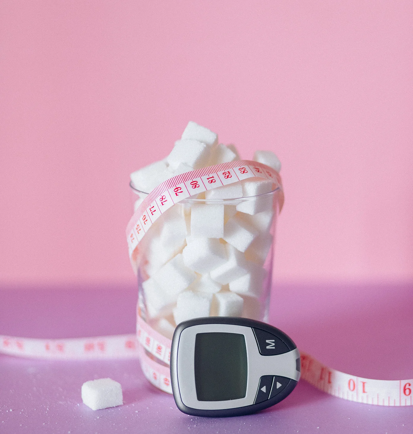 Zuckermessgerät neben einem Glas mit Zuckerwürfeln.